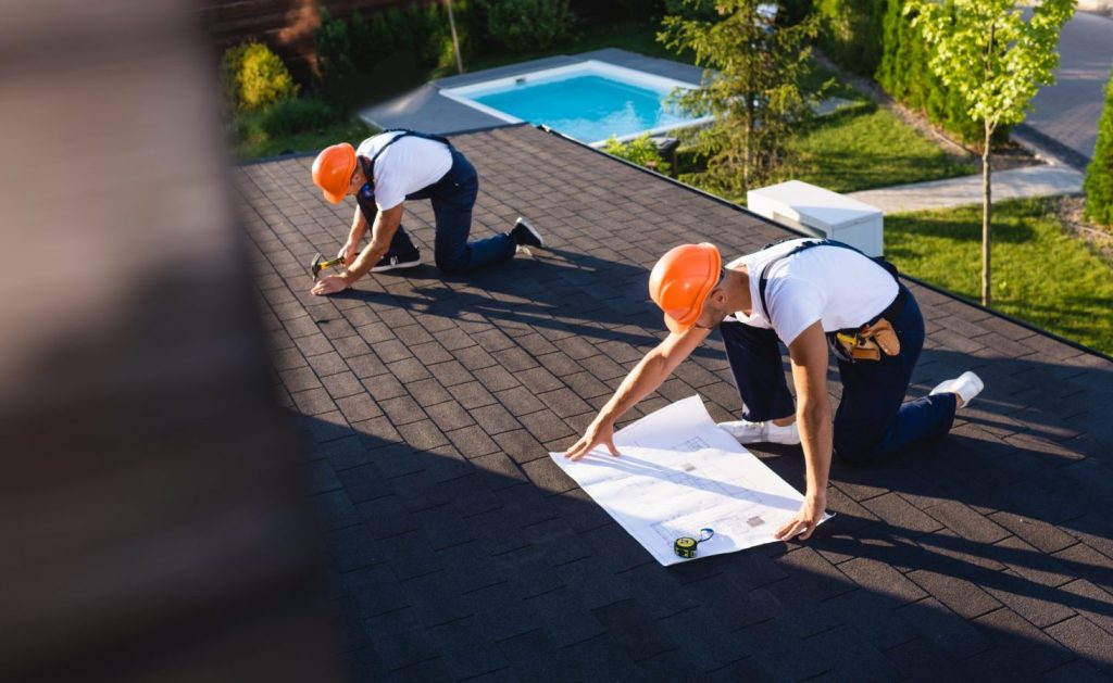 selective focus of builders with blueprint and tools working on roof of building